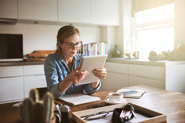 Young woman sitting at her kitchen table at home working on her small business with a digital tablet